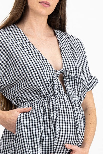 A pregnant woman modeling a black and white gingham wrap midi dress with short flutter sleeves, a tie waist, and a V-neckline, standing against a plain white studio background.